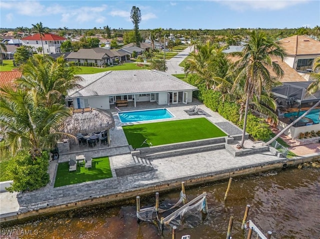 back of house featuring a water view, a patio area, boat lift, and a lawn