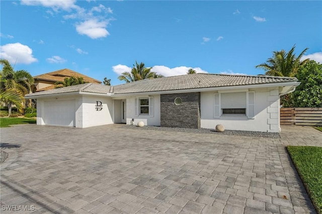 ranch-style house with decorative driveway, an attached garage, fence, stone siding, and a tiled roof