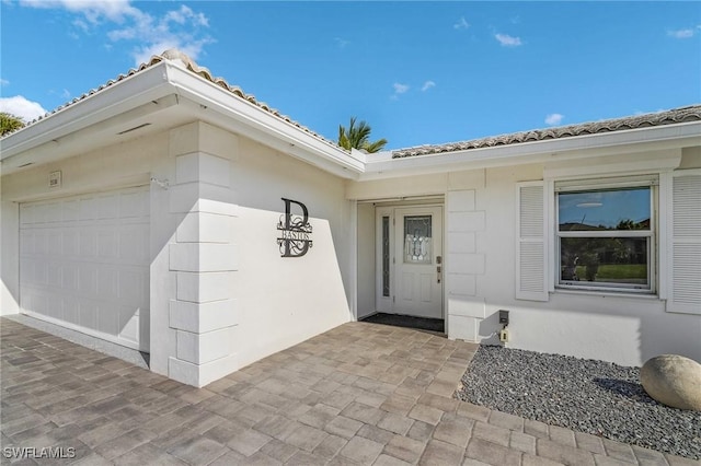 entrance to property featuring a garage, a tiled roof, and stucco siding