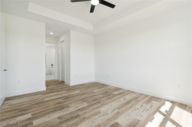 unfurnished room with light wood finished floors, baseboards, a tray ceiling, and a ceiling fan