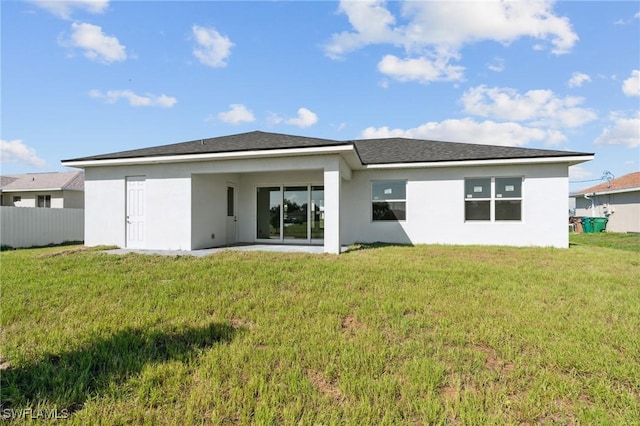 rear view of property featuring stucco siding, fence, and a yard