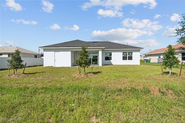 rear view of property with a lawn, fence, and stucco siding