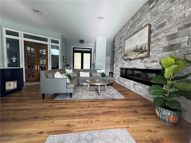 living area with visible vents, french doors, a stone fireplace, and wood finished floors