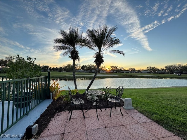 patio terrace at dusk with a water view and a yard