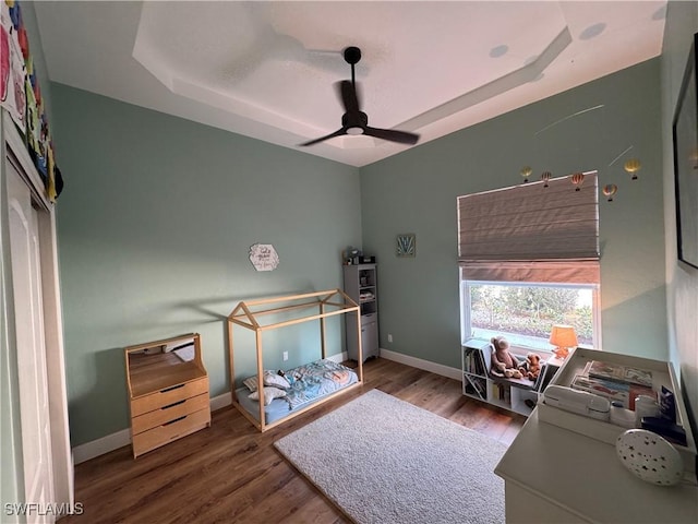 bedroom with a raised ceiling, wood finished floors, baseboards, and a ceiling fan