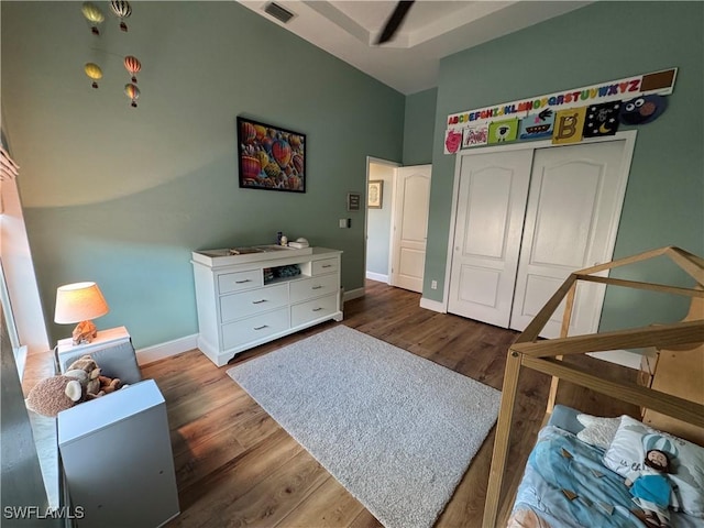 bedroom with wood finished floors, baseboards, a closet, and visible vents