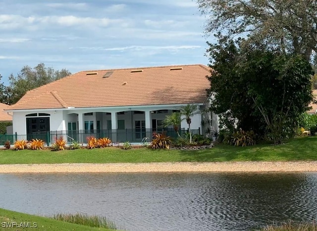rear view of property with a tiled roof, a yard, a water view, fence, and stucco siding