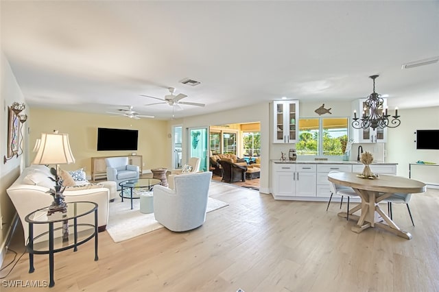 living area featuring light wood finished floors, visible vents, and ceiling fan with notable chandelier