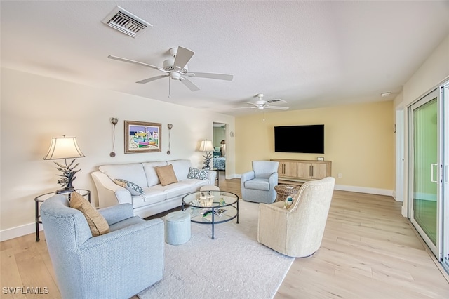 living room with a ceiling fan, visible vents, baseboards, light wood-style floors, and a textured ceiling