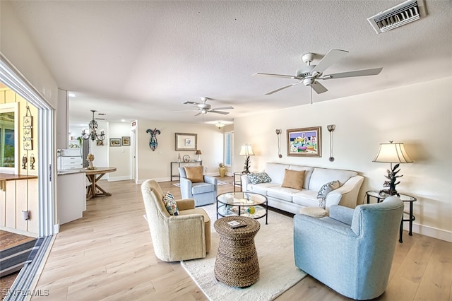 living area with visible vents, baseboards, ceiling fan, light wood-type flooring, and a textured ceiling