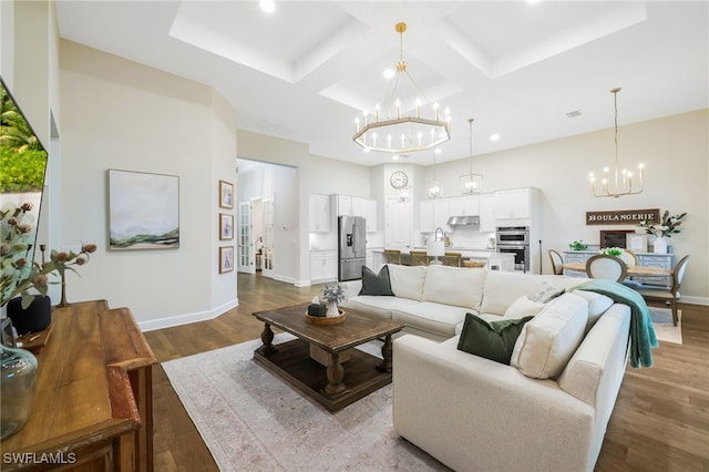 living area with baseboards, a chandelier, coffered ceiling, and wood finished floors