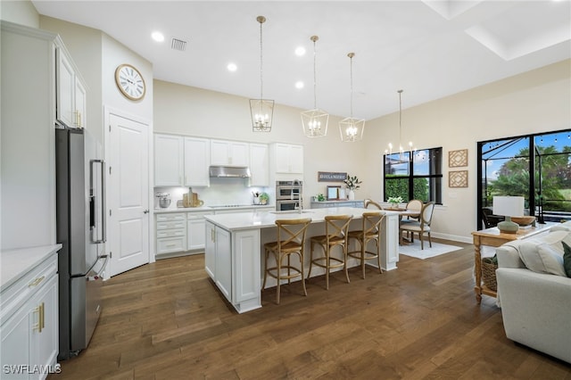 kitchen with dark wood finished floors, stainless steel appliances, visible vents, a high ceiling, and under cabinet range hood