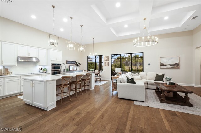 living area with dark wood finished floors, visible vents, a high ceiling, a chandelier, and coffered ceiling