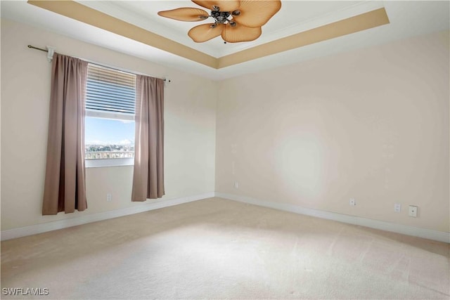 spare room featuring a raised ceiling, carpet flooring, ceiling fan, and baseboards