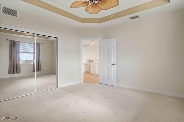 unfurnished bedroom featuring light carpet, a sink, visible vents, and a tray ceiling