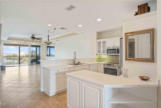 kitchen with a raised ceiling, appliances with stainless steel finishes, a peninsula, open shelves, and a sink