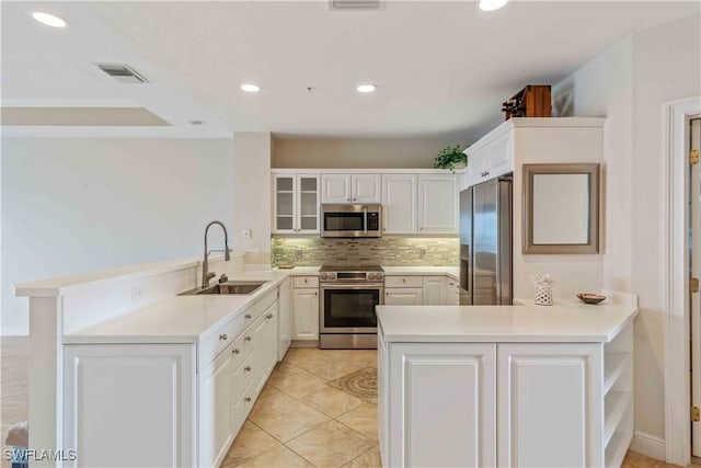 kitchen featuring stainless steel appliances, a peninsula, a sink, white cabinetry, and light countertops