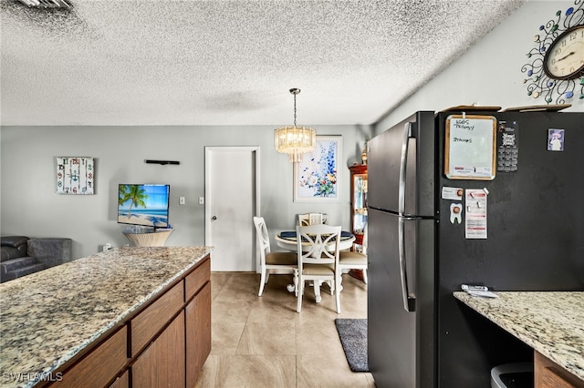 kitchen featuring brown cabinets, freestanding refrigerator, a textured ceiling, light stone countertops, and a chandelier