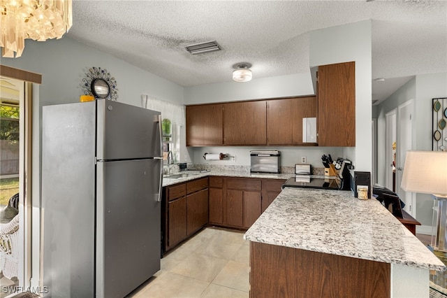 kitchen with visible vents, freestanding refrigerator, a peninsula, a textured ceiling, and a sink