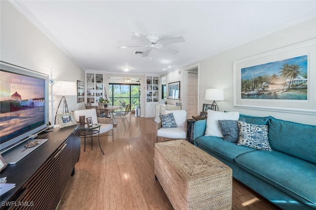 living area with ceiling fan, wood finished floors, visible vents, and crown molding