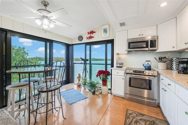 kitchen featuring lofted ceiling, light wood-style flooring, stainless steel appliances, visible vents, and decorative backsplash