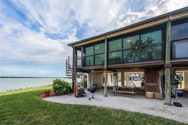 back of property with stairway, a lawn, and a water view