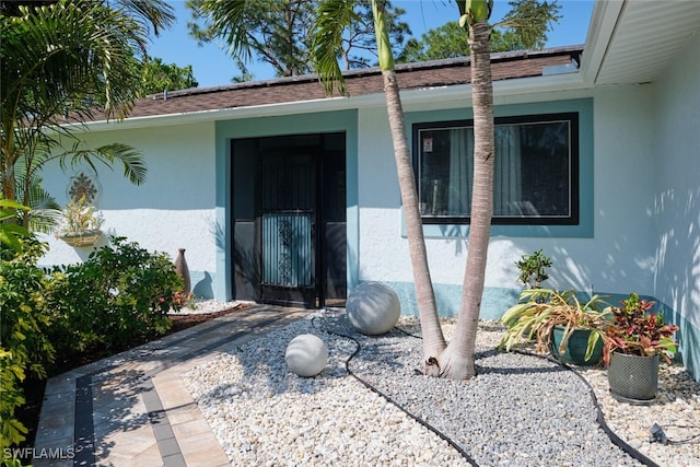 entrance to property featuring stucco siding and roof with shingles