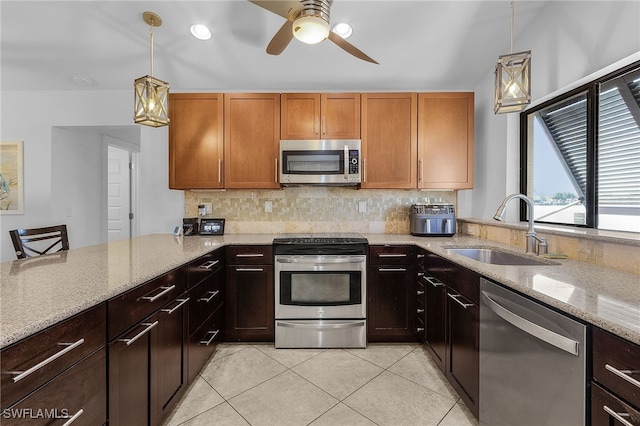 kitchen featuring stainless steel appliances, tasteful backsplash, a sink, light stone countertops, and a peninsula