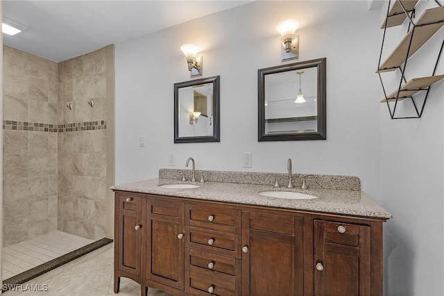 bathroom with double vanity, tiled shower, a sink, and tile patterned floors