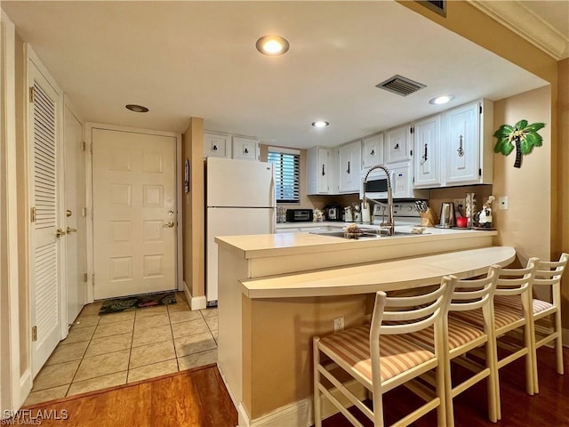 kitchen featuring light countertops, visible vents, freestanding refrigerator, white cabinetry, and a peninsula