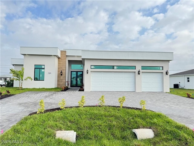 contemporary home with a garage, cooling unit, french doors, decorative driveway, and stucco siding