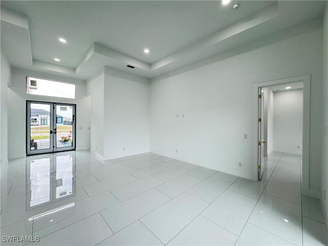 empty room with french doors, a raised ceiling, and recessed lighting