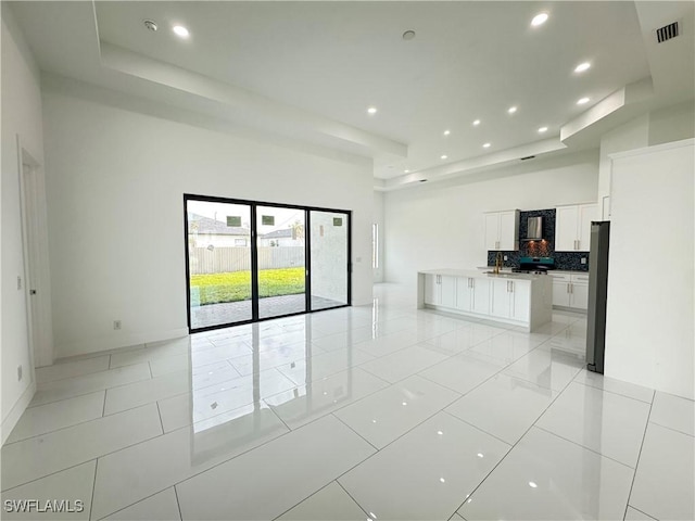 unfurnished living room with a tray ceiling, light tile patterned floors, recessed lighting, visible vents, and a high ceiling