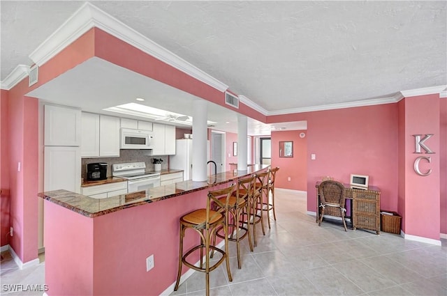 kitchen featuring a breakfast bar, crown molding, visible vents, dark stone countertops, and white appliances