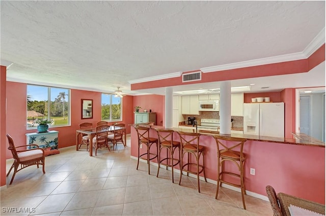 kitchen featuring ceiling fan, a breakfast bar area, white appliances, visible vents, and decorative backsplash