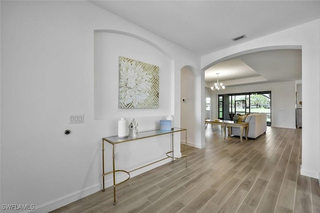 hallway with wood finished floors, visible vents, baseboards, an inviting chandelier, and a tray ceiling