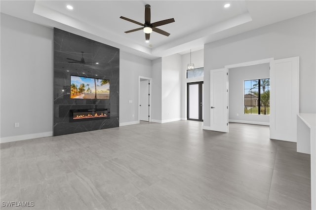 unfurnished living room with a tray ceiling, baseboards, and a high end fireplace