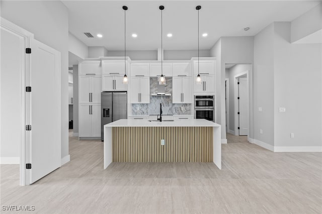 kitchen with an island with sink, stainless steel appliances, light countertops, white cabinetry, and wall chimney range hood