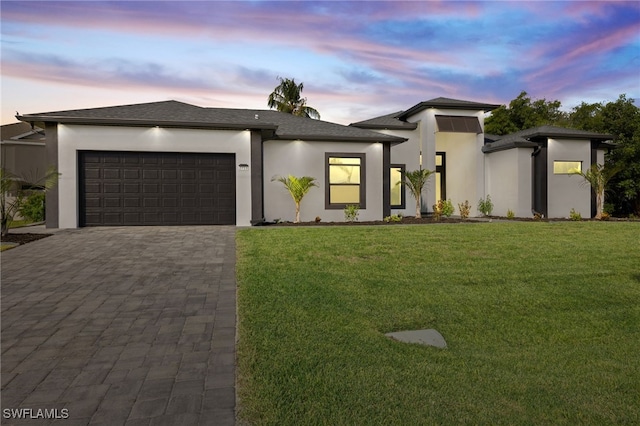 prairie-style house with a lawn, decorative driveway, a garage, and stucco siding