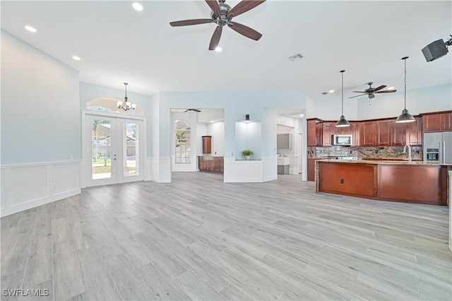 unfurnished living room with ceiling fan with notable chandelier, visible vents, french doors, wainscoting, and light wood-type flooring