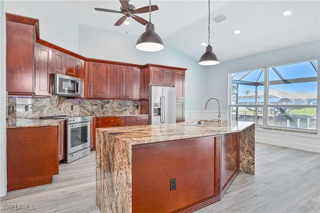 kitchen featuring stainless steel appliances, a sink, decorative backsplash, light stone countertops, and a center island with sink