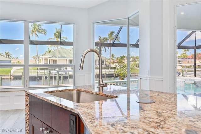 kitchen with a decorative wall, a water view, a sink, wainscoting, and light stone countertops