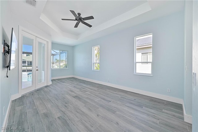 unfurnished room with french doors, a raised ceiling, visible vents, wood finished floors, and baseboards