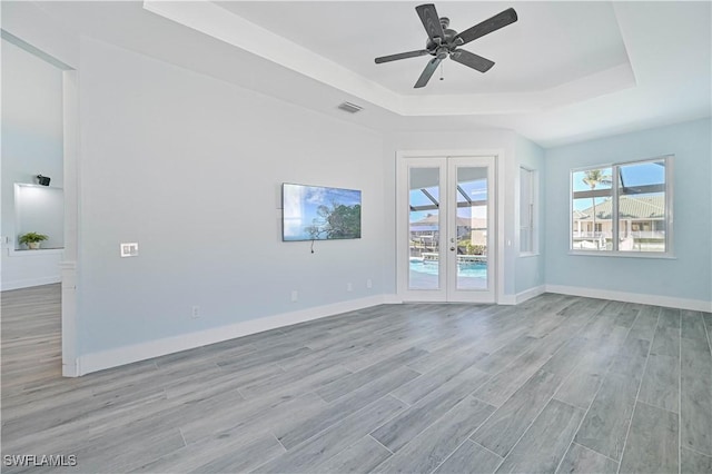 unfurnished living room with a tray ceiling, french doors, visible vents, light wood-style flooring, and baseboards