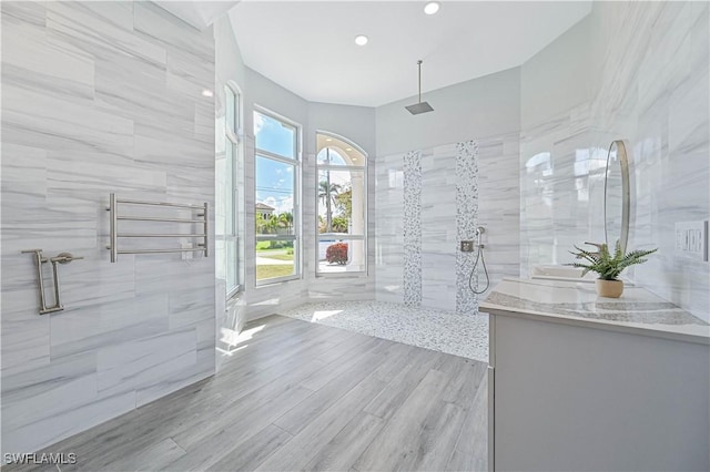 bathroom featuring wood finished floors, a walk in shower, tile walls, and vanity