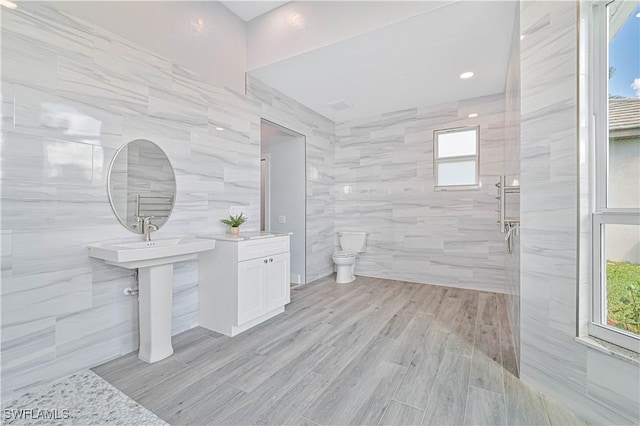 full bathroom featuring a tile shower, wood finished floors, a wealth of natural light, and tile walls