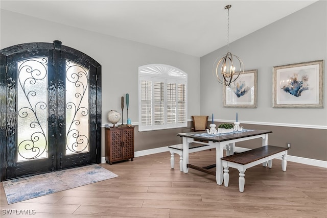 interior space with baseboards, light wood finished floors, an inviting chandelier, vaulted ceiling, and french doors