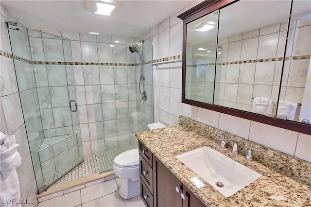 bathroom featuring toilet, vanity, tile walls, a shower stall, and tile patterned floors