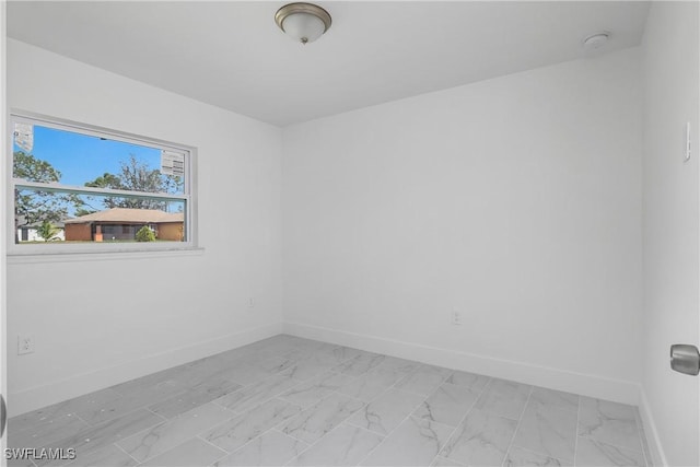 spare room featuring marble finish floor and baseboards