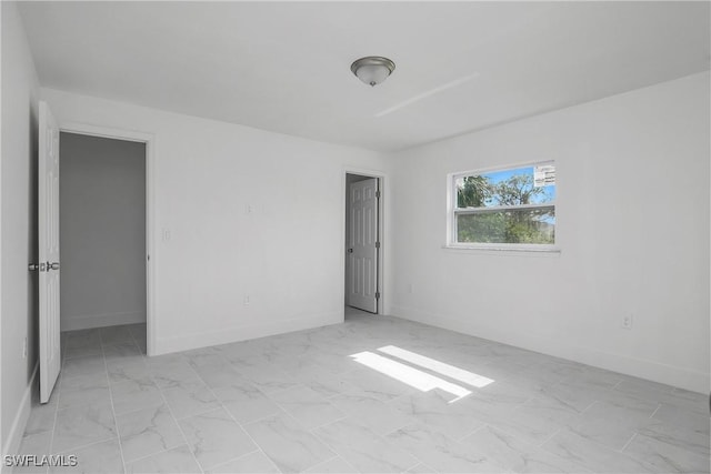 unfurnished room with marble finish floor and baseboards